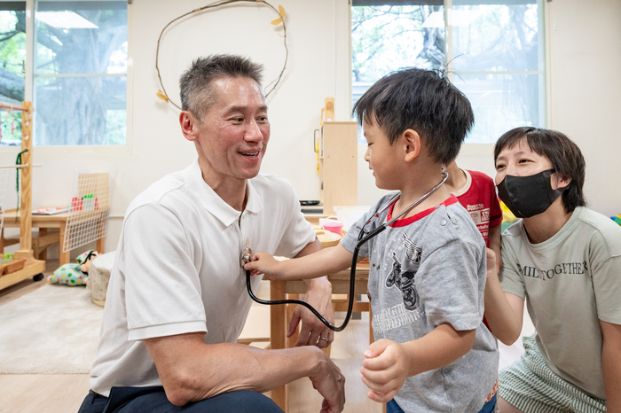 小朋友開心地扮起醫生，把聽診器貼在校長高為元胸前為他「看診」。